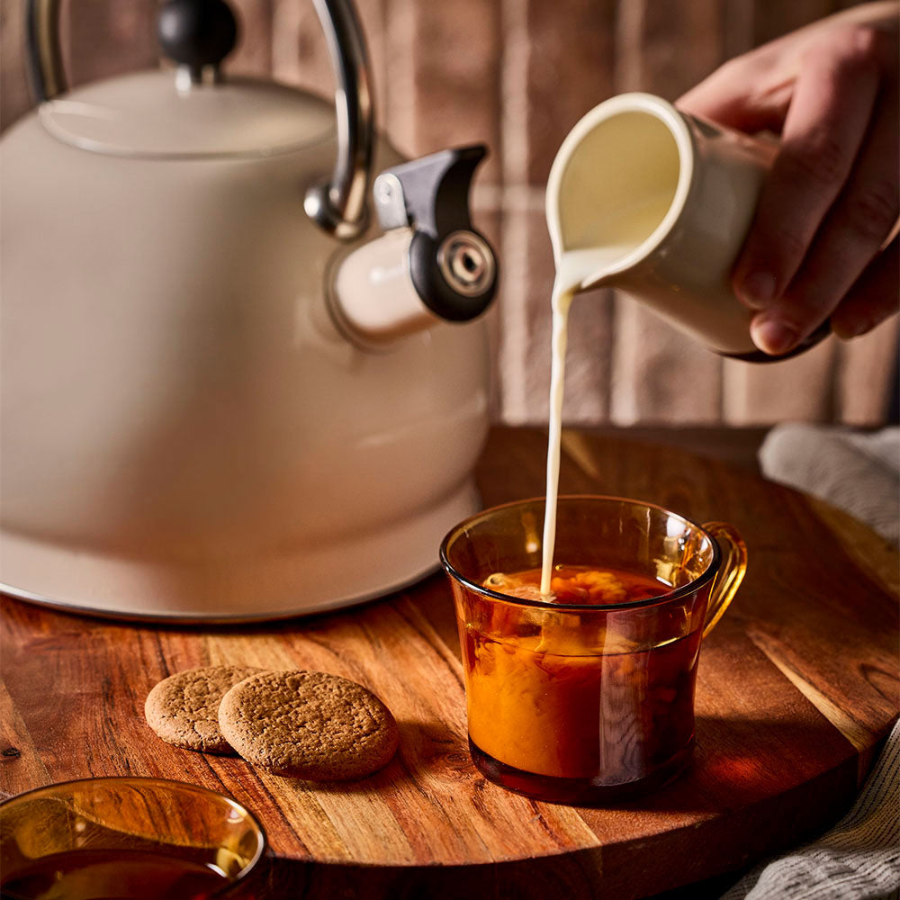 Cup of tea being topped with milk alongside the oat stovetop kettle.