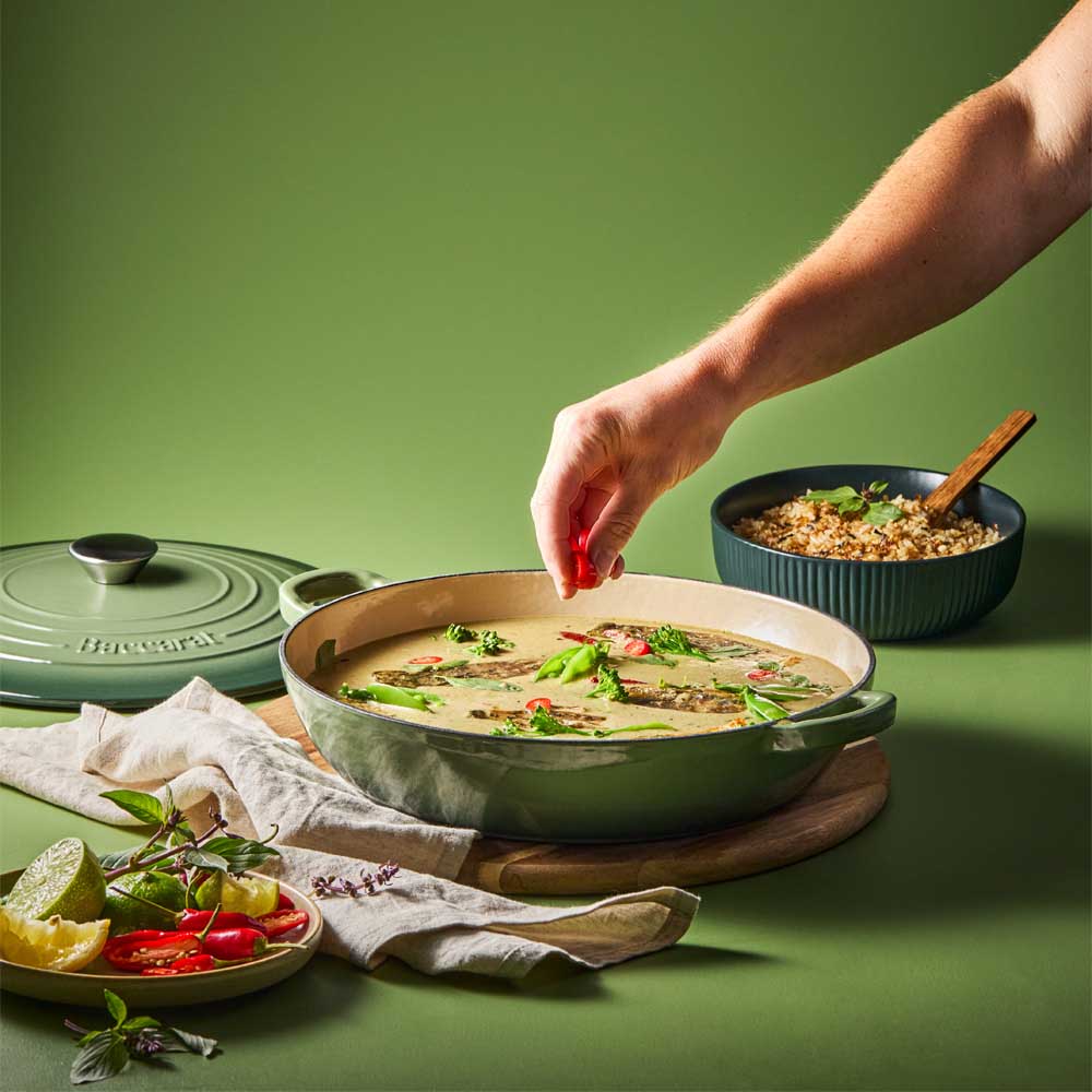 man sprinkling chilli into curry in green saute pan - Robins Kitchen